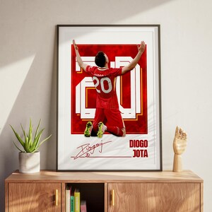 Pode incluir: P&ocirc;ster emoldurado com um jogador de futebol em uniforme vermelho, n&uacute;mero 20, ajoelhado com os bra&ccedil;os levantados. O p&ocirc;ster inclui a assinatura do jogador e o nome "DIOGO JOTA" em texto branco sobre fundo vermelho.