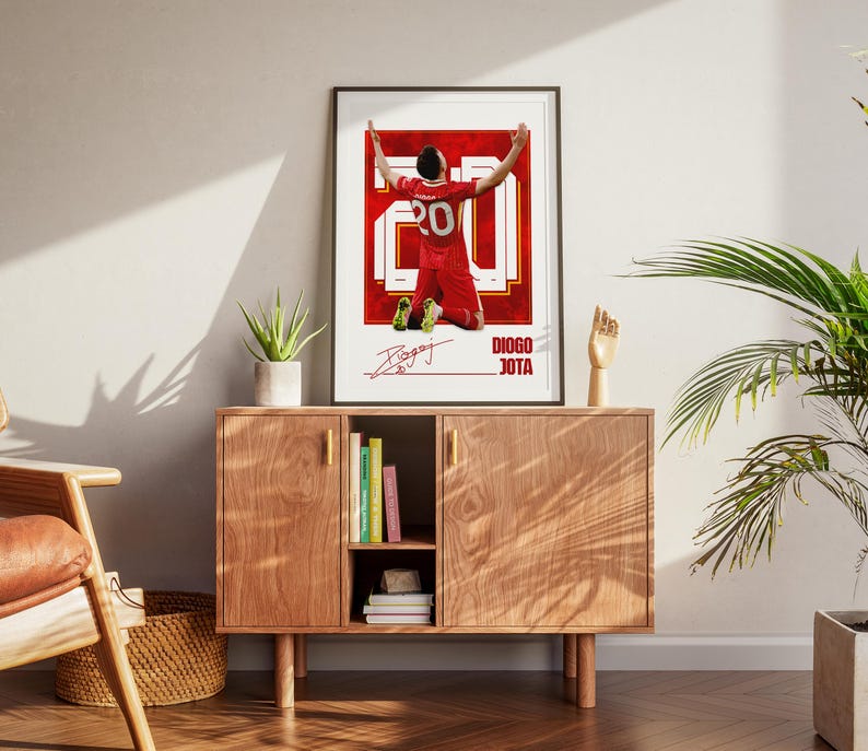 Pode incluir: Um poster emoldurado com um jogador de futebol de uniforme vermelho, ajoelhado com os bra&ccedil;os levantados. O poster tem um design vermelho e branco, o n&uacute;mero 20 e uma assinatura. O texto "DIOGO JOTA" tamb&eacute;m &eacute; vis&iacute;vel.