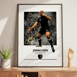 Könnte beinhalten: Gerahmter Druck mit einem Rugby-Spieler in schwarzer Uniform vor einem dunklen, abstrakten Hintergrund. Der Druck enthält den Namen "JONAH LOMU", eine Unterschrift und ein Schild-Grafik. Der Spieler ist in Aktion, mit einem Arm erhoben.