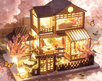 May include: A miniature wooden Japanese-style house with interior lighting, featuring a detailed design with multiple rooms, a small garden, and a traditional gate. The scene is adorned with pink cherry blossom branches, butterflies, and small birds.