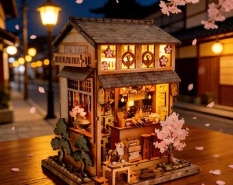 May include: A miniature wooden Japanese restaurant model with interior lighting. The model features a detailed facade, a small bar, and a miniature Shiba Inu figure. Cherry blossom accents and a street scene backdrop enhance the aesthetic.