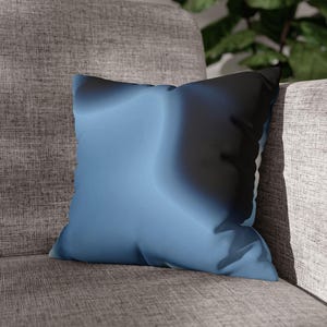 Peut inclure: Un coussin carré décoratif avec un motif dégradé. Le coussin passe du bleu clair au bleu foncé et au noir. Le coussin est posé sur une chaise rembourrée grise.