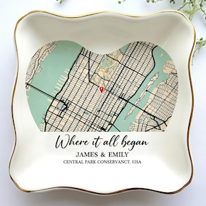May include: A white ceramic trinket dish with a gold rim, featuring a map of New York City in a heart shape. The text "Where it all began" is written below the map, along with the names "JAMES & EMILY" and "CENTRAL PARK CONSERVANCY, USA."