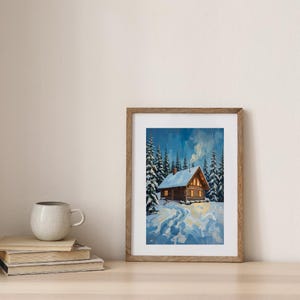Könnte beinhalten: Gerahmtes Gemälde eines gemütlichen Blockhauses in einem verschneiten Wald. Das Blockhaus hat ein schneebedecktes Dach und warme Lichter. Hohe immergrüne Bäume umgeben das Blockhaus, und ein Weg führt durch den Schnee. Der Himmel ist tiefblau.