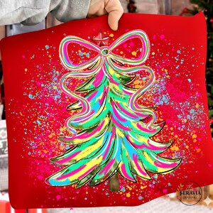 Puede incluir: Un cojín decorativo rojo con un diseño de árbol de Navidad colorido. El árbol está adornado con un lazo y una estrella, y está decorado con colores brillantes. El fondo tiene un efecto de salpicaduras.