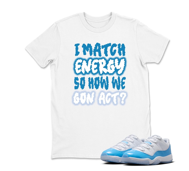 May include: White t-shirt with the text "I MATCH ENERGY SO HOW WE GON ACT?" in blue cloud-like font. A pair of white and light blue sneakers are in the foreground. The t-shirt and sneakers are likely part of a streetwear or casual fashion ensemble.