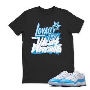 Peut inclure: T-shirt noir avec le texte "Loyalty Over Values Everything" en blanc et bleu clair. Une paire de baskets bleu clair et blanches est au premier plan.