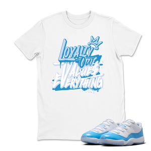 Peut inclure: T-shirt blanc avec l'inscription "Loyalty Over Values Everything" en bleu clair. Une paire de baskets bleu clair et blanches est au premier plan, assortie au design du t-shirt. L'ensemble t-shirt et baskets est coordonn&eacute;.