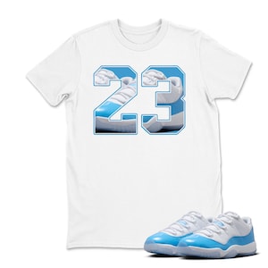 May include: White t-shirt with a blue outline of the number 23, filled with a photo of a blue and white sneaker. A pair of matching blue and white sneakers are in front of the shirt.