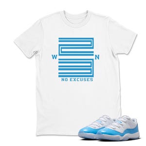 May include: White t-shirt featuring a blue graphic with the text "W 23 N NO EXCUSES." A pair of white and light blue trainers are in the foreground. The t-shirt is a casual style.