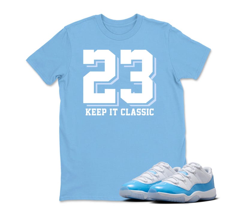Puede incluir: Una camiseta azul claro con el n&uacute;mero 23 en blanco y la frase "KEEP IT CLASSIC". Un par de zapatillas deportivas azules y blancas est&aacute;n delante de la camiseta.