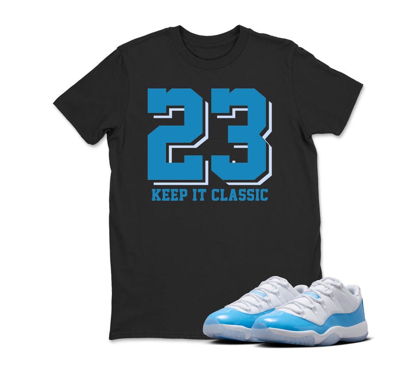 Puede incluir: Camiseta negra con el n&uacute;mero 23 en azul y blanco, con el texto "KEEP IT CLASSIC". Un par de zapatillas deportivas azules y blancas est&aacute;n delante de la camiseta.