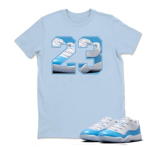 May include: A light blue t-shirt with the number "23" in a white and light blue design. The number is filled with an image of a light blue and white sneaker. A pair of light blue and white sneakers are in front of the shirt.