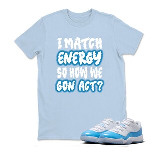May include: Light blue t-shirt with the text "I MATCH ENERGY SO HOW WE GON ACT?" in white and blue. A pair of light blue and white sneakers are in the foreground.