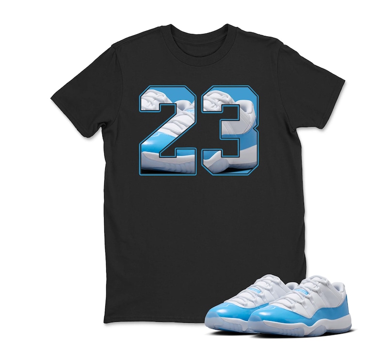 May include: Black t-shirt featuring the number "23" in a light blue and white design, with a pair of matching light blue and white sneakers in the foreground. The shirt's graphic incorporates an image of the sneakers.