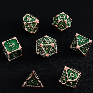 May include: A set of seven polyhedral dice featuring a deep green enamel inlay surrounded by intricate rose gold metal filigree. Each die displays embossed numbers and dragon-themed patterns on its faces, including a twenty-sided die showing the number 20.