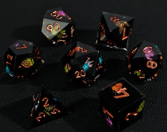 May include: Set of seven black polyhedral dice with copper-colored numbers and colorful floral and insect inclusions. The dice are designed for tabletop role-playing games and are displayed on a dark surface.