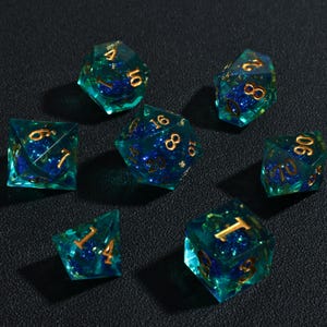 May include: Set of seven polyhedral dice. Each die is a translucent teal color with gold numbering and a dark blue interior. The dice are designed for tabletop role-playing games.