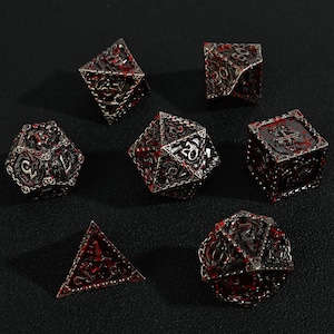 May include: Set of seven metal dice in various geometric shapes. The dice are silver with red accents and intricate filigree designs. The dice are for role-playing games.