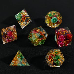 May include: Set of seven polyhedral dice with colorful flowers encased in clear resin. The dice have gold-colored numbers and are designed for tabletop role-playing games. The dice include a d4, d6, d8, d10, d12, d20, and a percentile die.
