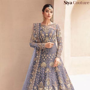 May include: A floor-length grey gown featuring intricate gold embroidery throughout the bodice, long sleeves, and full skirt. The garment includes a matching sheer grey dupatta draped over one shoulder, with Siya Couture text visible.
