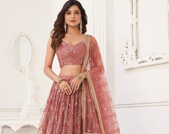 Op de afbeelding: Een stofroze lehenga choli set. De mouwloze top en lange rok zijn versierd met zilverkleurige geometrische patronen. Een bijpassende doorschijnende dupatta met gouden rand maakt de set compleet. De tekst "Siya Couture" is rechtsboven zichtbaar.