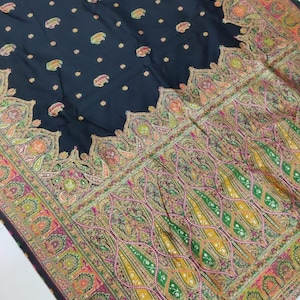 May include: A dark navy shawl with an intricate paisley pattern in shades of green, yellow, pink, and orange. The border features a detailed floral design, and the shawl has a fringe trim.