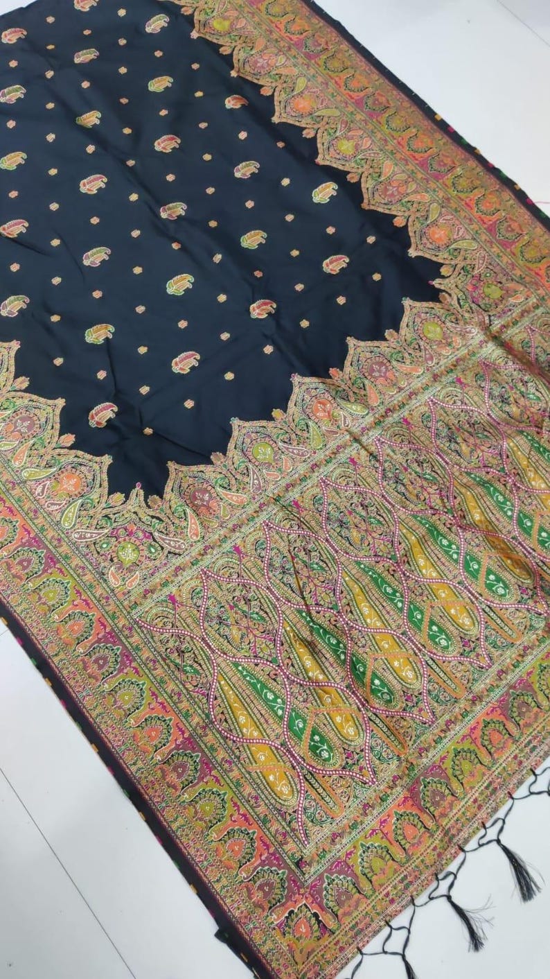 May include: A dark navy shawl with an intricate paisley pattern in shades of green, yellow, pink, and orange. The border features a detailed floral design, and the shawl has a fringe trim.