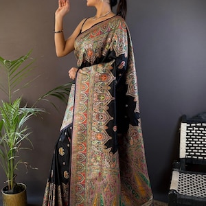 May include: A black sari with intricate, colorful embroidery. The sari features a detailed paisley pattern in shades of red, green, yellow, and orange. The garment is draped over a person, showcasing the design and texture of the fabric.