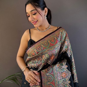 May include: Black sari with a colorful paisley pattern. The sari features a detailed design with shades of red, green, orange, and yellow. The sari is draped over the shoulders.