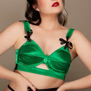 May include: A green satin bra with black bows on the straps. The cups have a circular, quilted design.