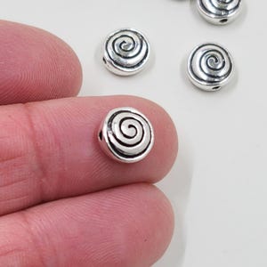 May include: Silver metal beads with a spiral design. The beads are round and have a hole in the centre for stringing.