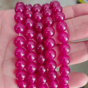 May include: A strand of deep pink round beads. The beads are smooth and glossy, and they are strung on a clear thread.