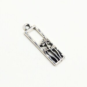 May include: Silver charm featuring a rectangular frame with a detailed design of three mushrooms inside.