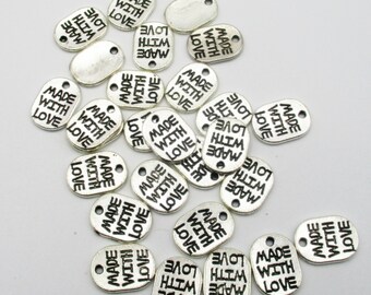 May include: A collection of silver oval-shaped metal tags with the text "Made with Love" printed on them. The tags have a hole at the top for stringing or attaching.