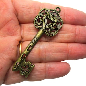 May include: A large, ornate, antique-style key with a heart-shaped design in the centre of the bow. The key is made of metal and has a bronze finish.