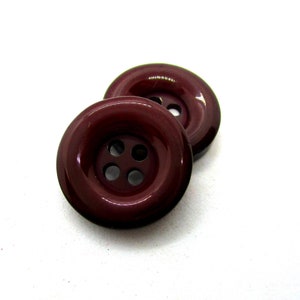 Peut inclure: Deux boutons en plastique marron avec quatre trous chacun.