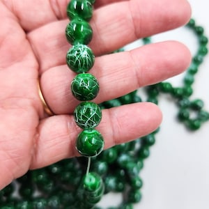 May include: A strand of green glass beads with white crackle detailing. The beads are round and have a glossy finish.