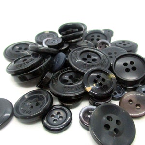 May include: A collection of black plastic buttons with various sizes and designs. Some buttons have the words "HIGH-MINDED" printed on them.