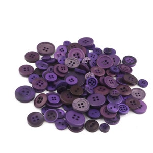 May include: A large assortment of purple buttons in various sizes and styles. The buttons are made of plastic and have a smooth, shiny finish.