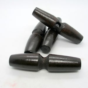 May include: A collection of dark brown wooden toggle buttons. Each button has a cylindrical shape with a rounded end and a central groove. The buttons are arranged on a white surface, showcasing their smooth, polished finish.