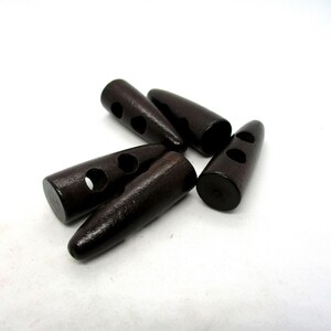 Peut inclure: Cinq boutons à bascule en bois brun foncé avec deux trous chacun. Les boutons ont la forme d'un ovale pointu.