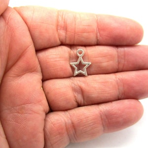 May include: A small, silver star charm with a loop for attaching to jewellery. The star has a five-point design with an open centre. This charm is ideal for necklaces, bracelets, or earrings.