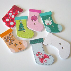 May include: Six wooden Christmas stocking buttons with various holiday designs. The designs include a red and white polka dot stocking, a green stocking with a Christmas tree, a pink stocking with a Christmas ornament, a green stocking with a reindeer, an orange stocking with stars, and a white stocking with a candy cane.