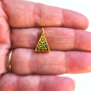 May include: A gold-coloured triangle pendant with an intricate design. The pendant has a loop at the top for attaching to a chain or cord.