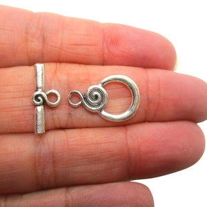 May include: Silver tone toggle clasp with a spiral design. The clasp is made of metal and has a polished finish.