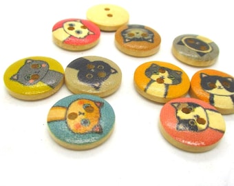 May include: Assortment of wooden buttons with cat faces printed on them. The buttons are in various colors, including yellow, orange, blue, red, and gray.