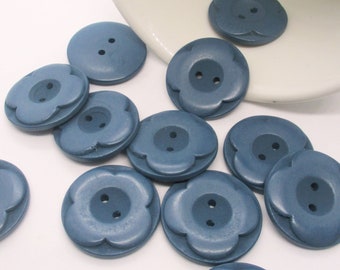 May include: A collection of 12 blue wooden buttons with a flower shape and two holes. The buttons are arranged on a white surface.
