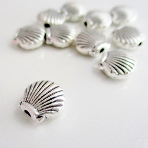 May include: A group of silver metal seashell charms, some are stacked on top of each other, and one is laying flat on a white surface.