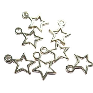 May include: Silver star charms with a hollow centre and a small loop at the top for stringing. These charms are suitable for jewellery making, scrapbooking, or other craft projects. The charms are scattered on a white background.